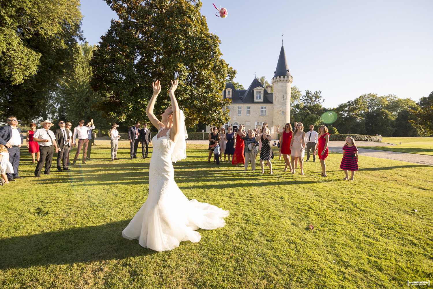 La mariée en belle robe blanche lance son bouquet de fleurs le jour de son mariage à Bordeaux dans le jardin du parc devant le chateau Agassac à Ludon-Médoc